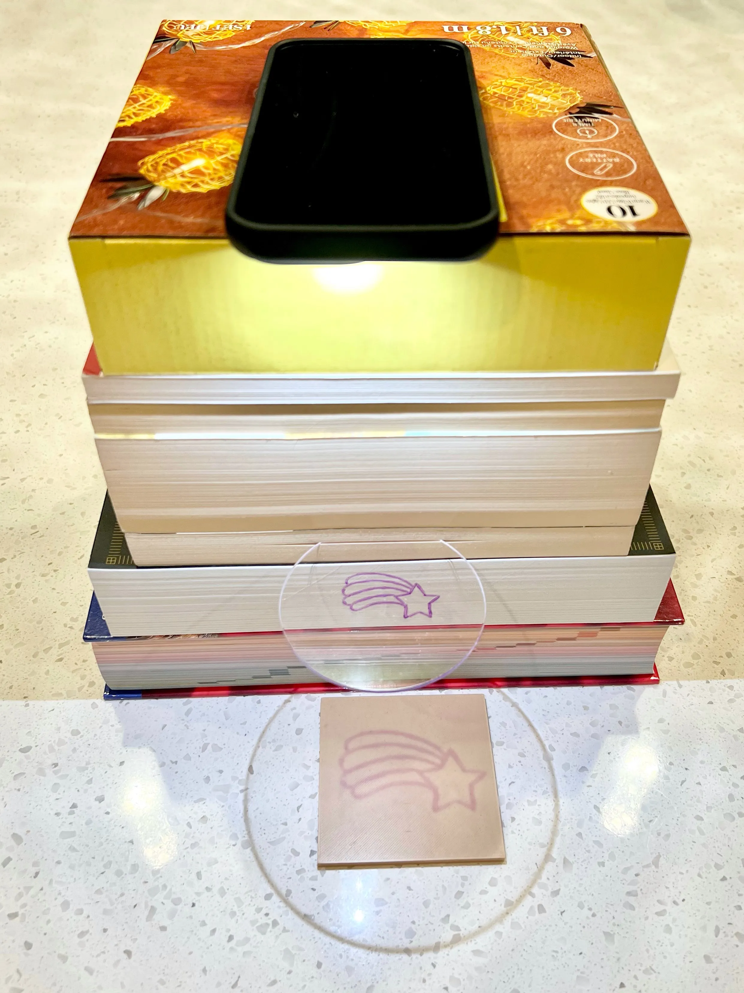 Phone flashlight on a stack of books with the acrylic circle positioned to project the design